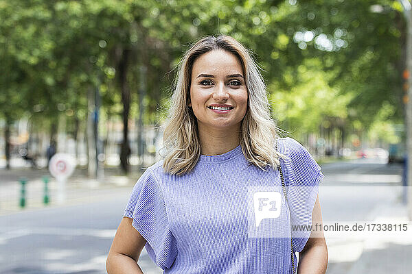 Lächelnde junge Frau mit blondem Haar auf der Straße stehend