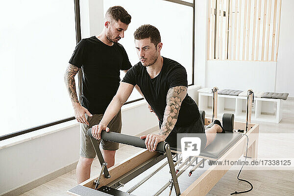 Male instructor guiding man exercising in pilates studio