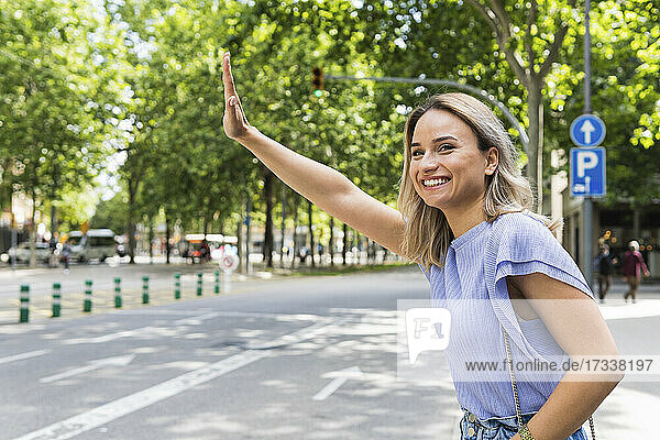 Lächelnde junge Frau  die auf der Straße ein Taxi ruft