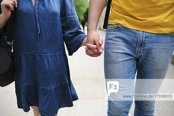Junges Paar hält sich beim gemeinsamen Spaziergang im Park an den Händen