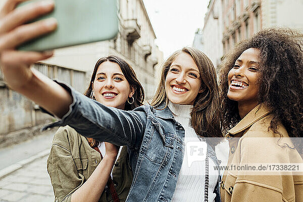 Cheerful friends taking selfie through mobile phone