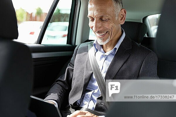 Smiling businessman using laptop in car