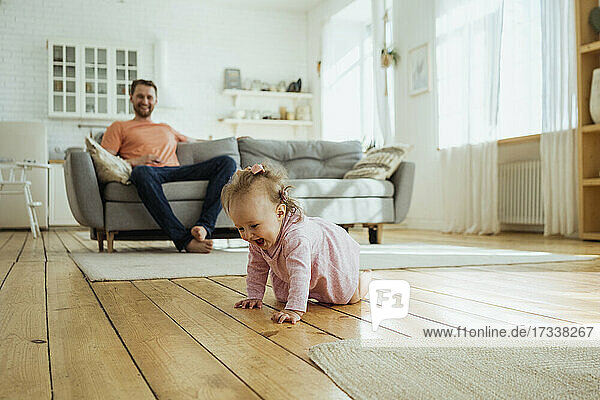 Mann sieht seine Tochter zu Hause auf dem Boden krabbeln
