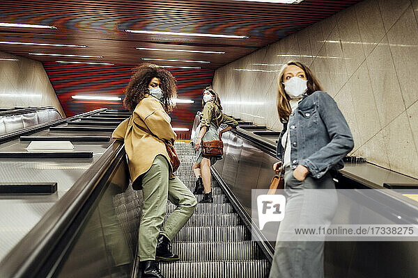 Freunde mit Gesichtsschutz  die in sozialer Distanz auf der Rolltreppe stehen