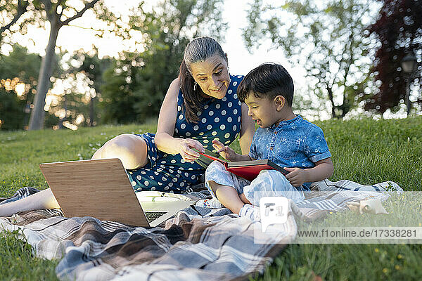 Excited woman assisting boy reading story book in public park