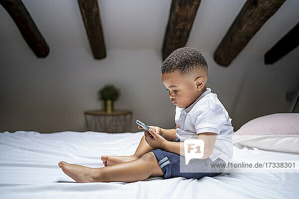 Boy using smart phone while sitting on bed at home