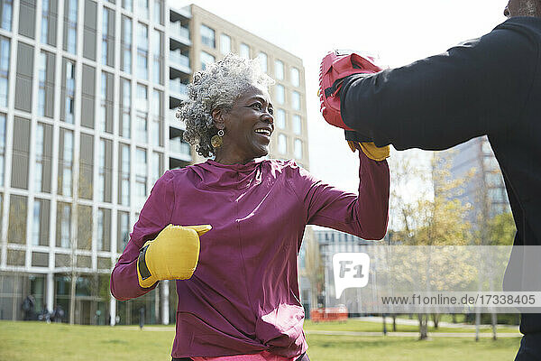Lächelnde Frau übt mit einem Mann im Park an einem sonnigen Tag Boxen