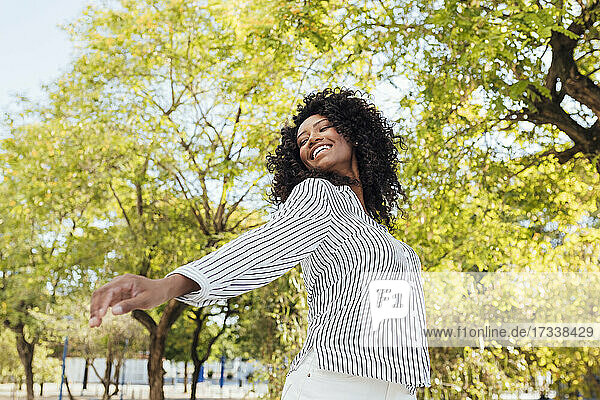 Glückliche Frau mit lockigem Haar tanzt im Park