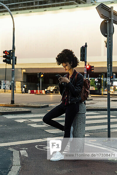 Young woman using mobile phone while leaning on bollard