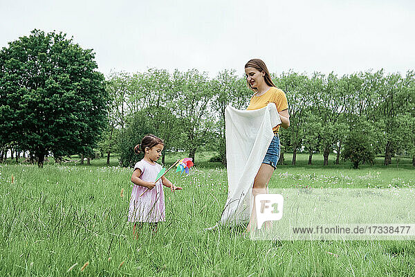 Tochter mit Windrad in der Nähe der Mutter mit Decke im Park stehend