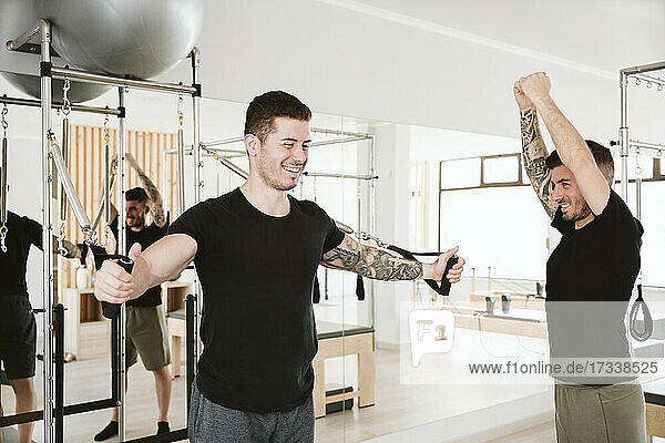 Smiling male instructor assisting man exercising in pilates studio