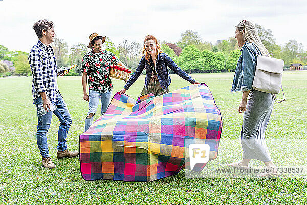 Young woman with picnic blanket doing preparation with friends at meadow