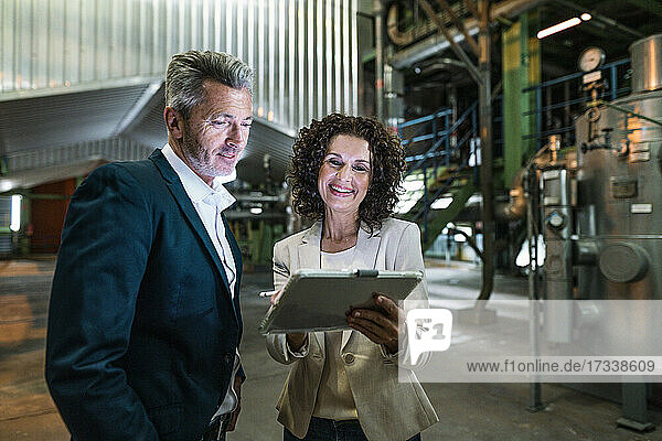 Fröhliche Geschäftsfrau zeigt einem Kollegen in der Industrie ein digitales Tablet