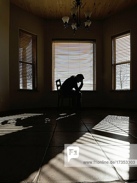 Silhouette of depressed man sitting on chair in living room
