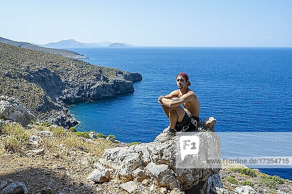 Junger Mann sitzt auf einem Felsen an der Küste  Kalymnos  Dodekanes  Griechenland  Europa
