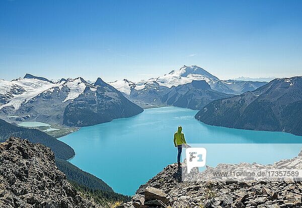 Junger Mann steht auf einem Felsen  blickt in die Ferne  Blick auf Berge und Gletscher mit türkisblauem See Garibaldi Lake  Gipfel Panorama Ridge  Guard Mountain und Deception Peak  Garibaldi Provincial Park  British Columbia  Kanada  Nordamerika