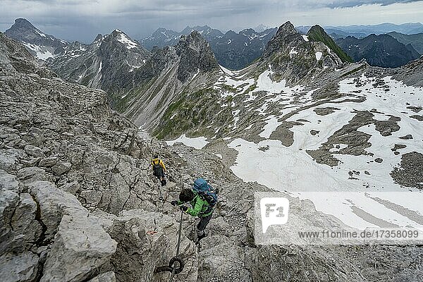 Hiker and hiker descending rocky terrain  path secured with steel rope  in the background mountain panorama with old snow fields and rocky mountain peaks  Heilbronner Weg  Allgäu Alps  Allgäu  Bavaria  Germany  Europe