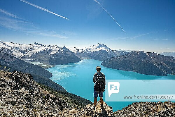 Young man standing on a rock  looking into the distance  view of mountains and glacier with turquoise blue lake Garibaldi Lake  peaks Panorama Ridge  Guard Mountain and Deception Peak  Garibaldi Provincial Park  British Columbia  Canada  North America