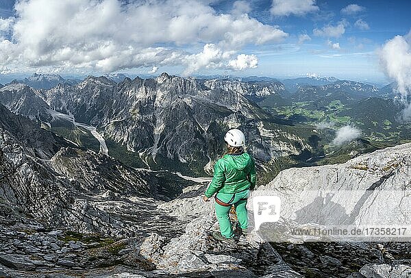 Wanderin mit Helm am Gipfel des Watzmann  Ausblick über Berge  Gebirgszug Hochkalterstock mit Blaueisspitze und Hochkalter  Wanderweg zum Watzmann  Watzmann-Überschreitung  Berchtesgaden  Bayern  Deutschland  Europa