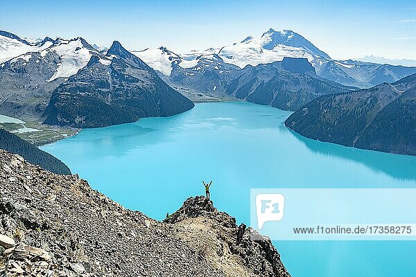 Young man standing on a rock  stretching his arms in the air  view of mountains and glacier with turquoise blue lake Garibaldi Lake  peaks Panorama Ridge  Guard Mountain and Deception Peak  Garibaldi Provincial Park  British Columbia  Canada  North America