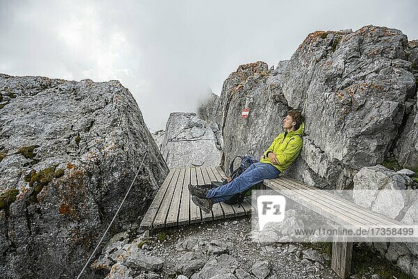 Hiker sits tired on a bench and sleeps  hiking trail to the Watzmann  Watzmann crossing  Berchtesgaden  Bavaria  Germany  Europe