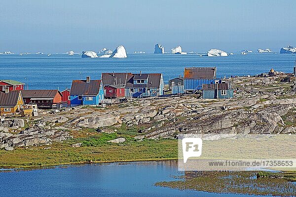 Holzhäuser und Felsen vor einer mit Eisbergen gefüllten Bucht  Diskobucht  Diskoinsel  Qeqertarsuaq  Arktis  Grönland  Dänemark  Nordamerika