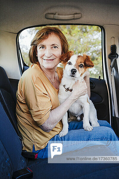 Frau sitzt mit Hund auf dem Rücksitz eines Autos
