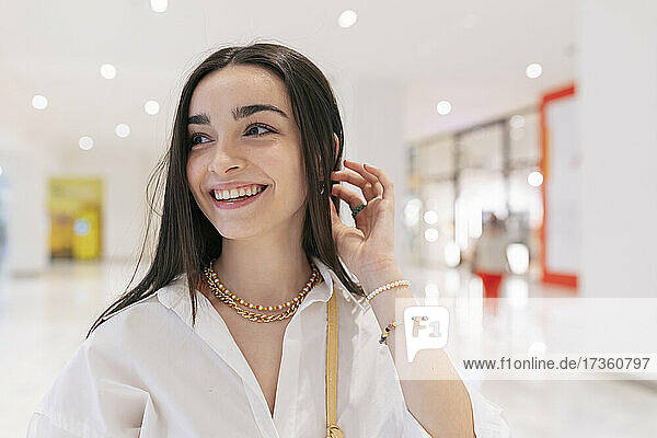 Lächelndes Teenager-Mädchen mit Hand im Haar  das im Einkaufszentrum wegschaut