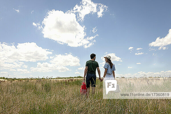 Couple holding bag while walking on meadow