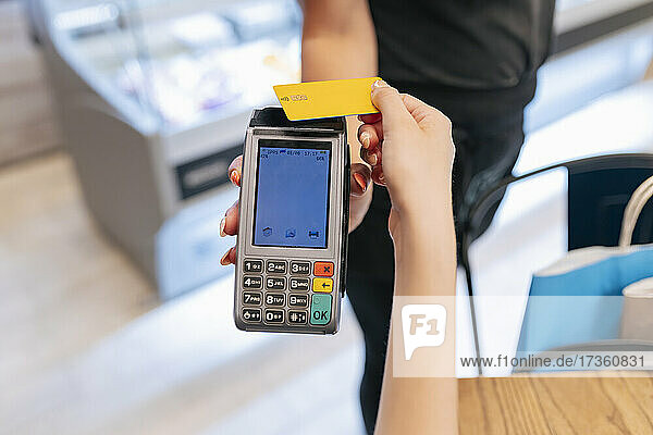 Frau hält Kreditkarte in der Hand  während sie bei einer Kellnerin im Food Court bezahlt