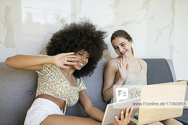Multiethnische Freundinnen winken während eines Videoanrufs auf einem digitalen Tablet zu Hause