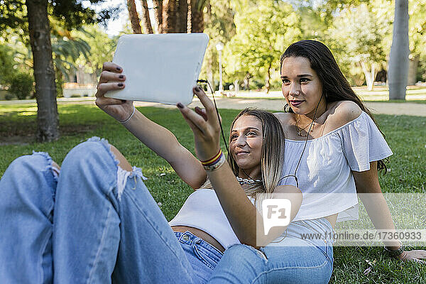 Junge Frau mit Freundin nimmt Selfie durch digitale Tablette im Park