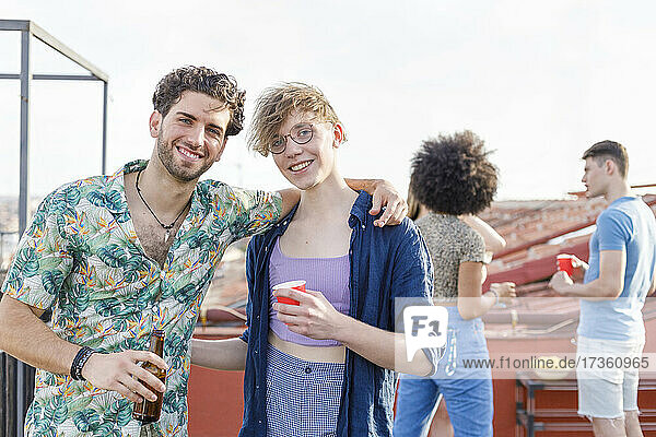 Smiling young friends having drinks on penthouse terrace