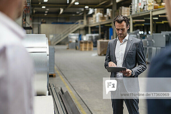 Geschäftsmann  der ein digitales Tablet benutzt  während er in der Nähe von Kollegen in einer Fabrik steht