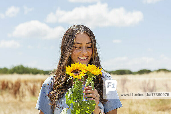 Lächelnde Frau betrachtet Sonnenblumen im Stehen an einem sonnigen Tag