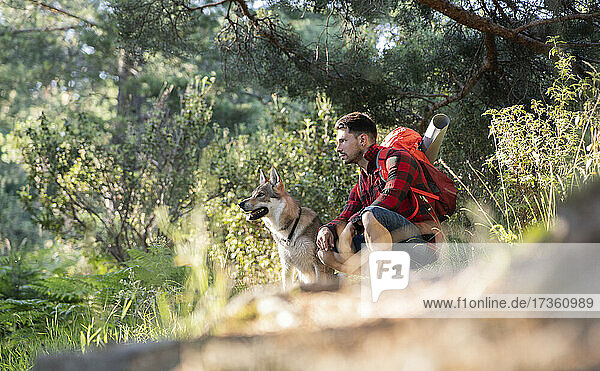 Mann mit Rucksack sitzt bei Hund im Wald
