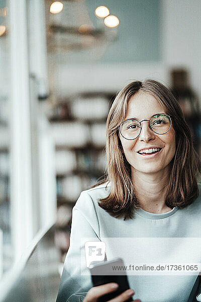 Happy young woman with brown hair wearing eyeglasses sitting in cafe