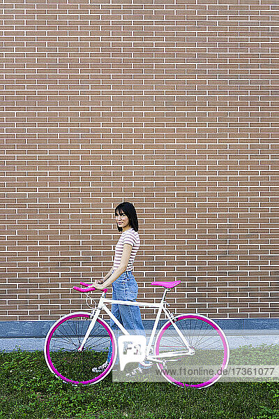 Frau mit Fahrrad geht an einer Mauer vorbei
