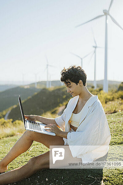 Lächelnde Frau  die einen Laptop benutzt  während sie auf einem Berg sitzt