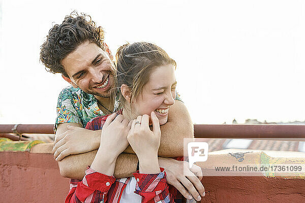 Junger Mann umarmt fröhliche Freundin auf dem Dach am Wochenende