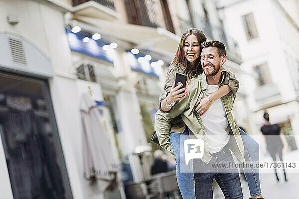 Fröhliche Frau  die ein Selfie mit ihrem Smartphone macht  während sie ihren Freund huckepack nimmt