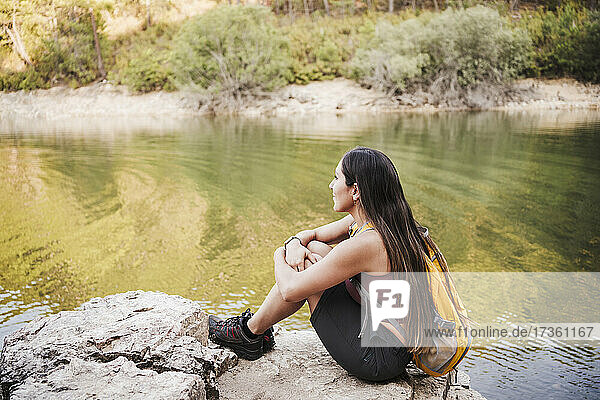 Weiblicher Rucksacktourist betrachtet die Aussicht  während er im Urlaub auf einem Felsen sitzt