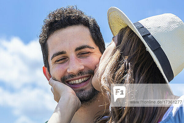 Freundin mit Hut küsst ihren Freund an einem sonnigen Tag