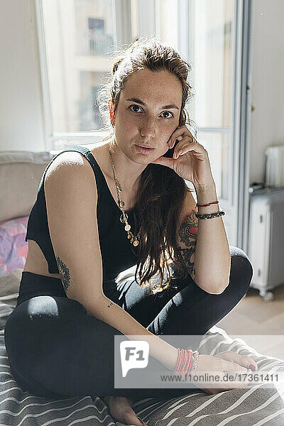 Woman staring while sitting cross-legged on bed in apartment