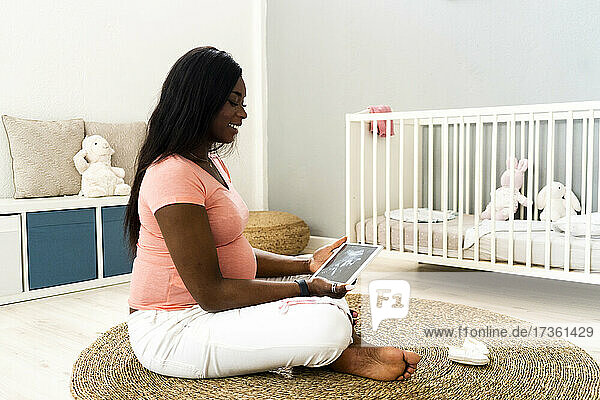 Glückliche schwangere Frau hält digitales Tablet mit Ultraschallvideo zu Hause