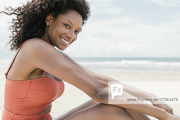 Glückliche junge Frau im Badeanzug am Strand sitzend