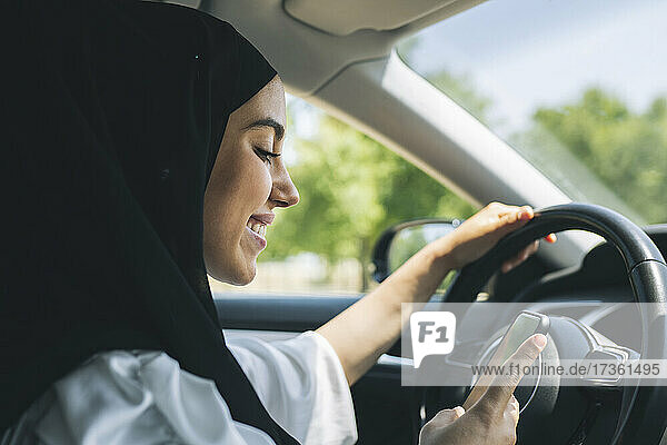 Lächelnde junge Frau  die im Auto ein Mobiltelefon benutzt