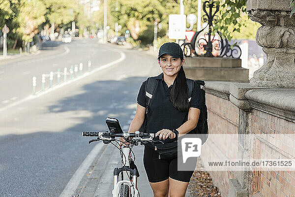 Lächelnde junge weibliche Zustellerin  die ein Fahrrad schiebt