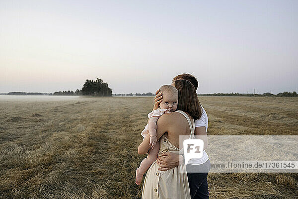 Mutter trägt süßes Mädchen  während sie neben einem Mann auf einem Feld steht