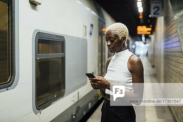 Junge Frau benutzt ein Mobiltelefon  während sie in einer U-Bahn-Station steht